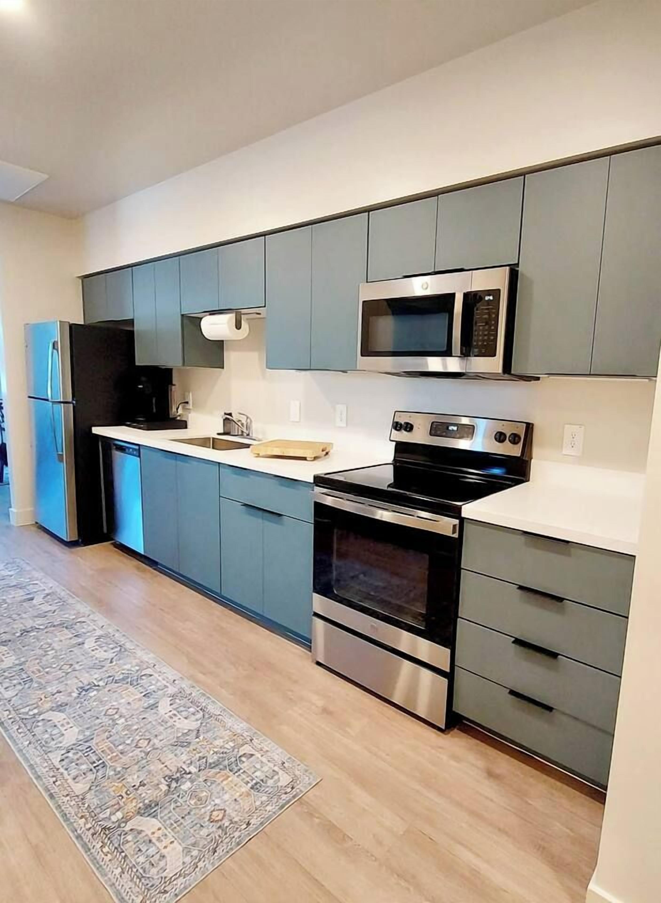 Une cuisine moderne avec des meubles gris, un four à micro-ondes, une cuisinière et un lave-vaisselle.
