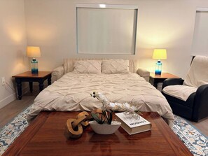 Een slaapkamer met een bed, twee nachtkastjes, een stoel, een houten vloer en een raam.