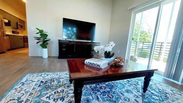 Een woonkamer met een houten salontafel, een flatscreen televisie, een plant in pot en uitzicht door een schuifdeur.
