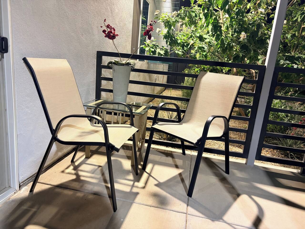 Een terras buiten met twee stoelen en een tafel, een hekwerk en uitzicht op groen.