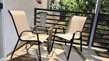 Een terras buiten met twee stoelen en een tafel, een hekwerk en uitzicht op groen.