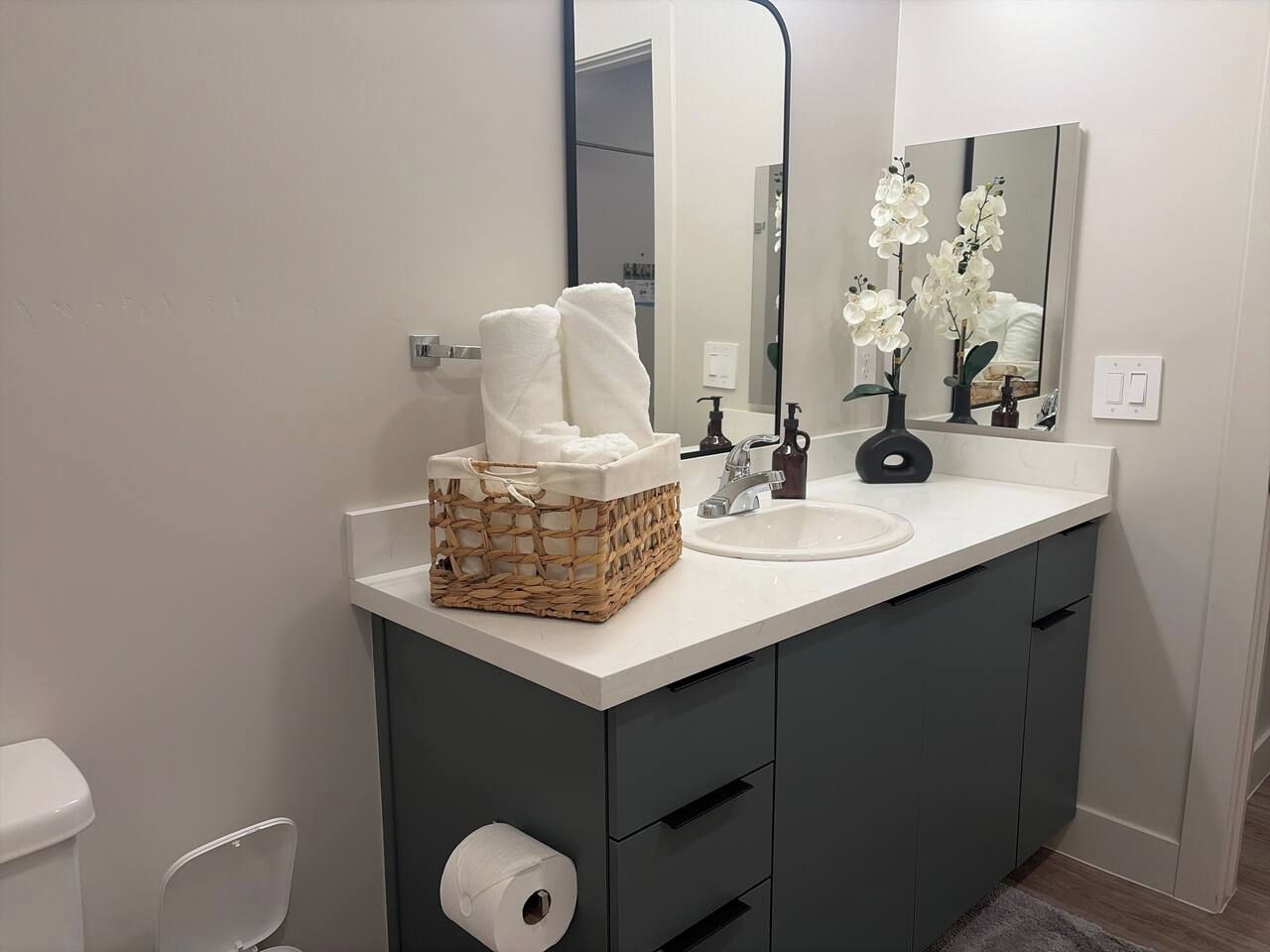 A bathroom with a white sink, dark cabinets, a mirror, and a basket of white towels.