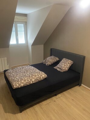 Un dormitorio con techo inclinado, una cama con ropa de cama estampada y una ventana con persianas.