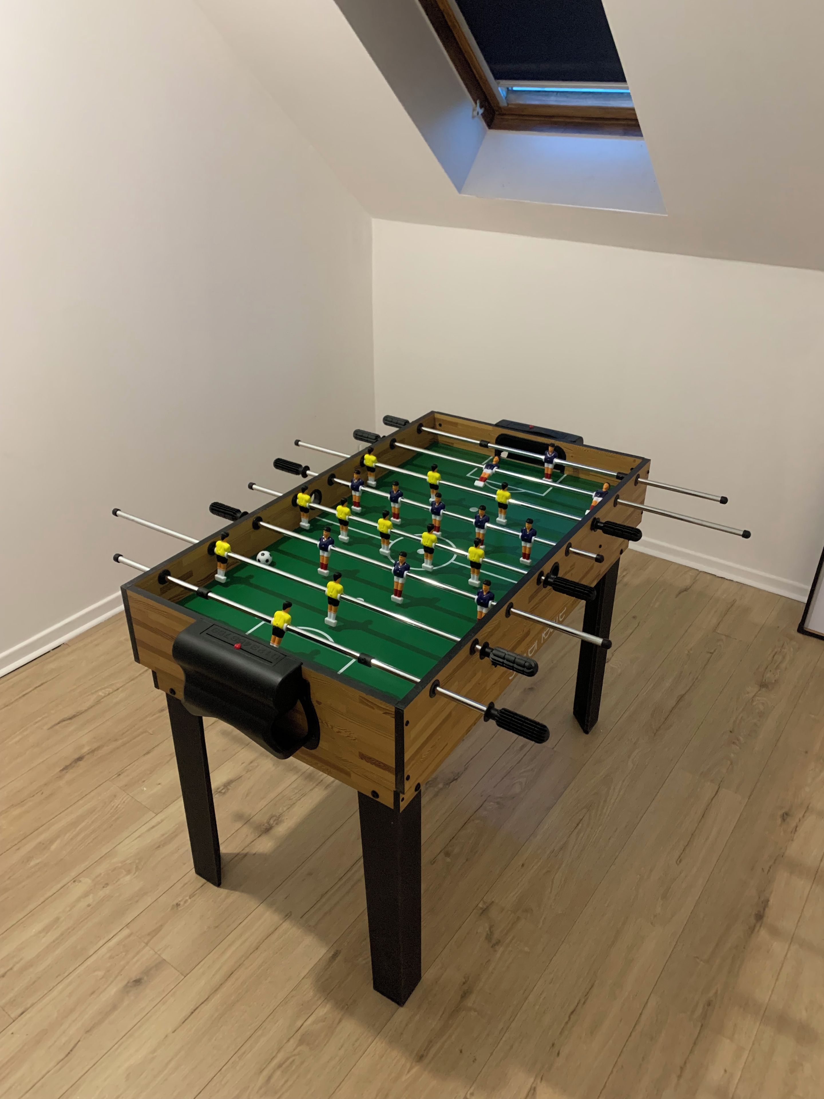 Une table de baby-foot dans une pièce dont le sol est en bois et dont le plafond est incliné.