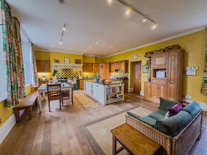 A spacious living area with a sofa, a dining table, and chairs. There is a kitchen area with wooden cabinets and a central island. - Eden Mount, Wetheral -  a cottage that sleeps 10 guests  in 5 bedrooms (Wetheral)