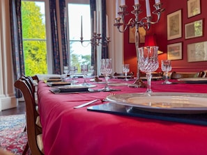 A dining table set with multiple wine glasses, plates, and cutlery, with a red tablecloth and a chandelier in the background. - Eden Mount, Wetheral -  a cottage that sleeps 10 guests  in 5 bedrooms (Wetheral)