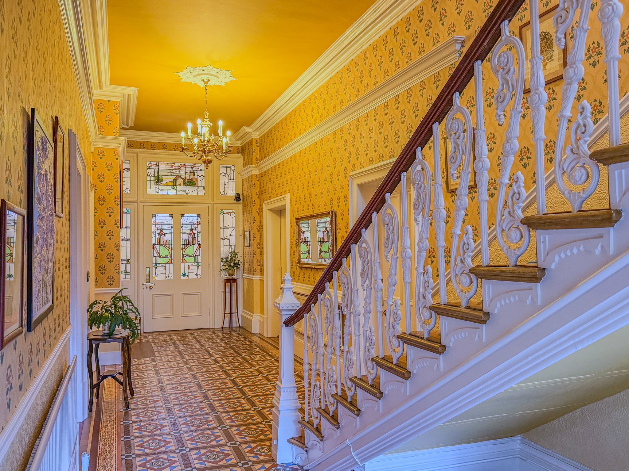 Un vaste hall d’entrée avec un sol à motifs, un escalier orné de balustrades travaillées et un lustre.