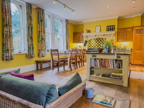 A cozy living room with a sofa, a dining table with chairs, a kitchen area with wooden cabinets, and a bookshelf filled with books. - Eden Mount, Wetheral -  a cottage that sleeps 10 guests  in 5 bedrooms (Wetheral)