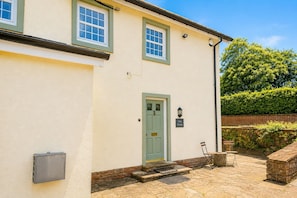 A two-story building with a green door, a small outdoor seating area with a table and chairs, and a sign on the wall. - Eden Grange, Wetheral, dog friendly cottage with stunning views (Wetheral)