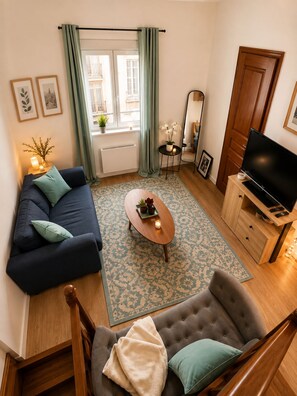 Una sala de estar con sofá, una mesa de centro, televisión y vistas al exterior.