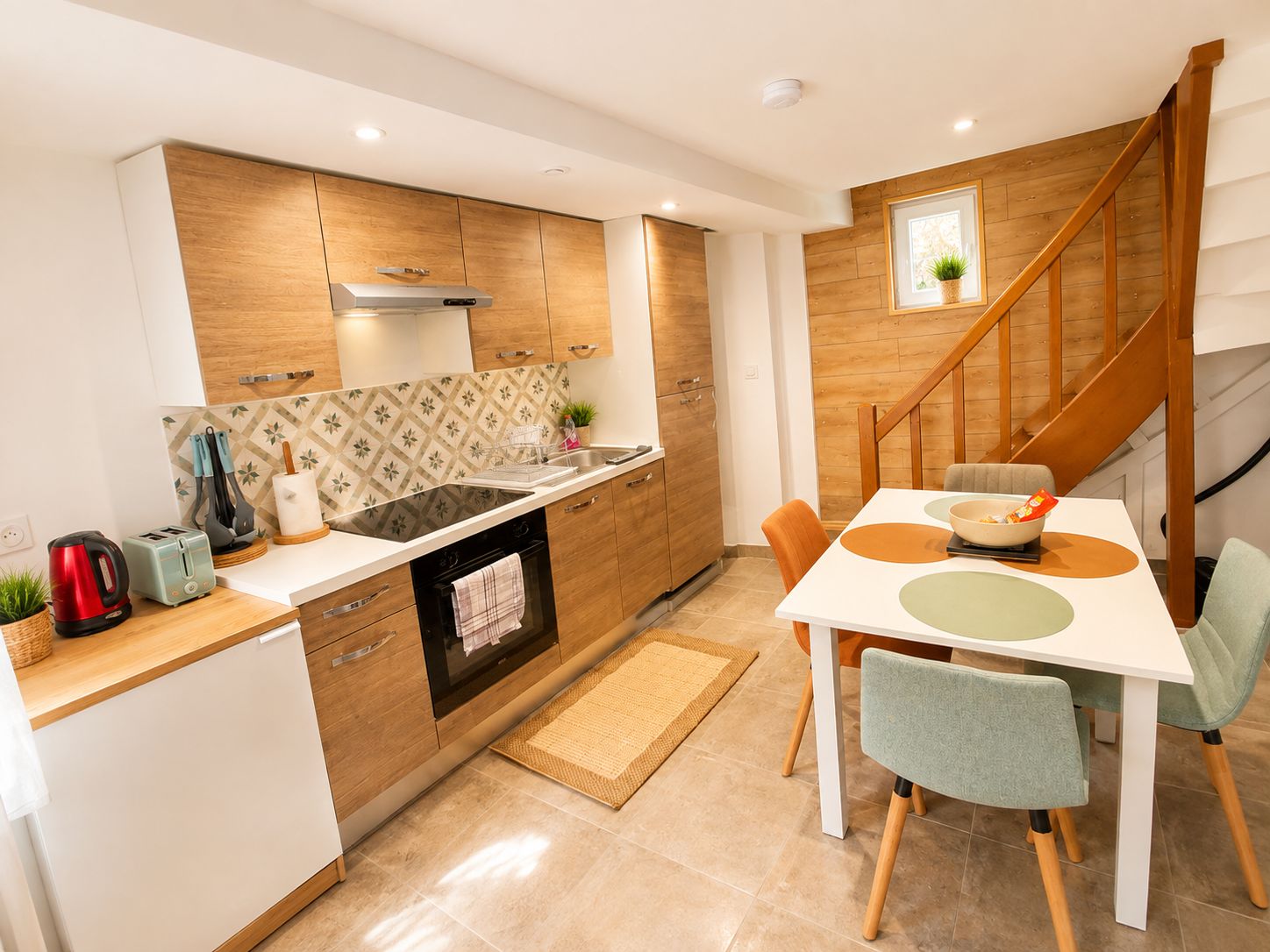 A modern kitchen with wooden cabinets, a built-in oven, and a dining area with a white table and chairs.