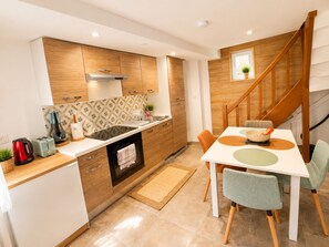 Una cocina moderna con armarios de madera, horno integrado y comedor con mesa y sillas blancas.