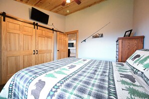 Quarto com cama grande, guarda-roupa de madeira e televisão montada na parede.