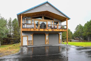 A two-story building with a balcony, large garage doors, and a covered front porch. - Cozy Cabin near Yellowstone! (Island Park)