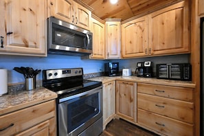 A kitchen with wooden cabinets, a stainless steel microwave, a stove, and a coffee maker. - Cozy Cabin near Yellowstone! (Island Park)