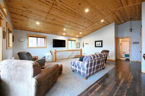 A cabin interior with a wooden ceiling, a sofa, a chair, a television, and a sign indicating the cabin number. - Cozy Cabin near Yellowstone! (Island Park)