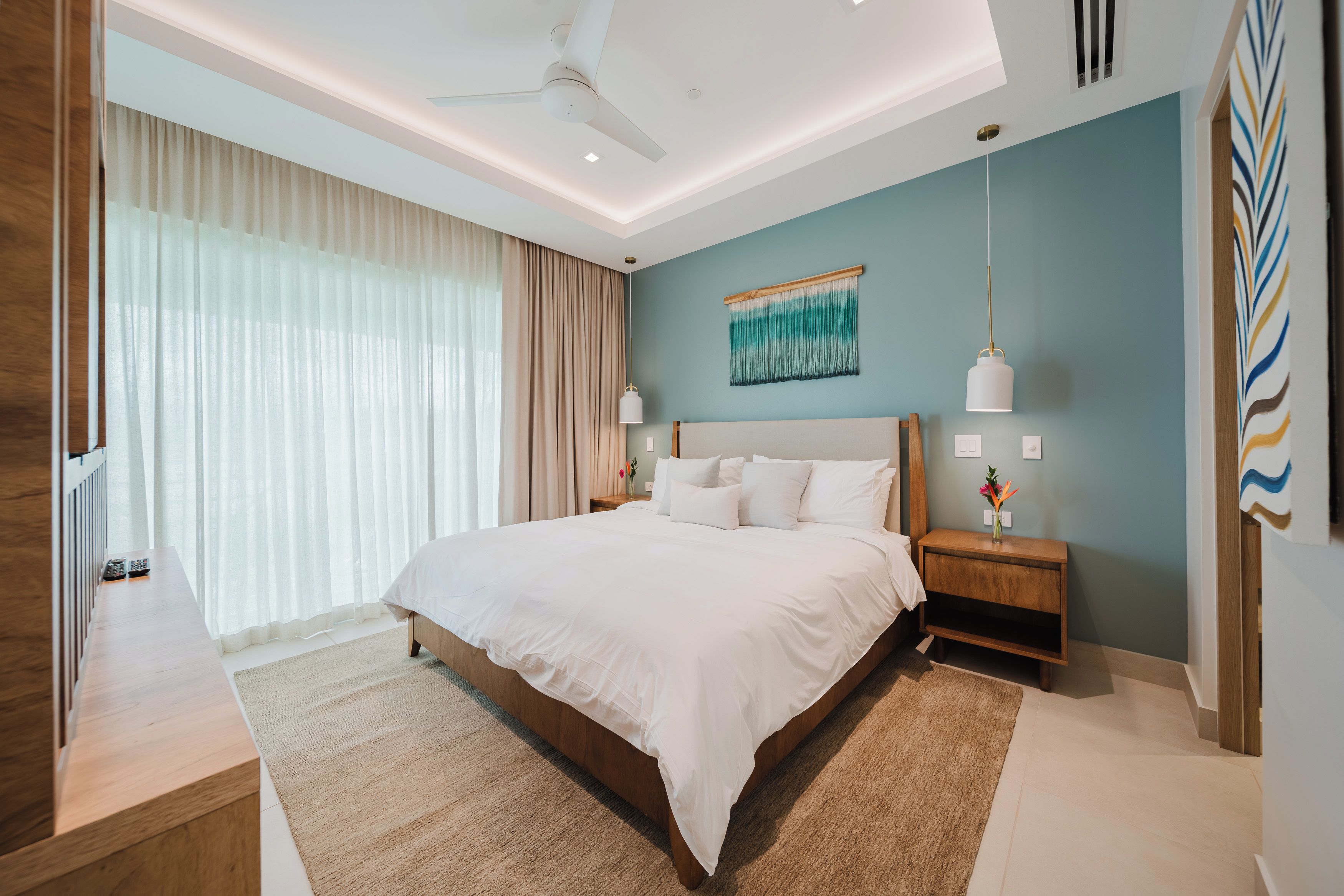 A modern bedroom with a large bed, bedside tables, a ceiling fan, and a wall-mounted light fixture.
