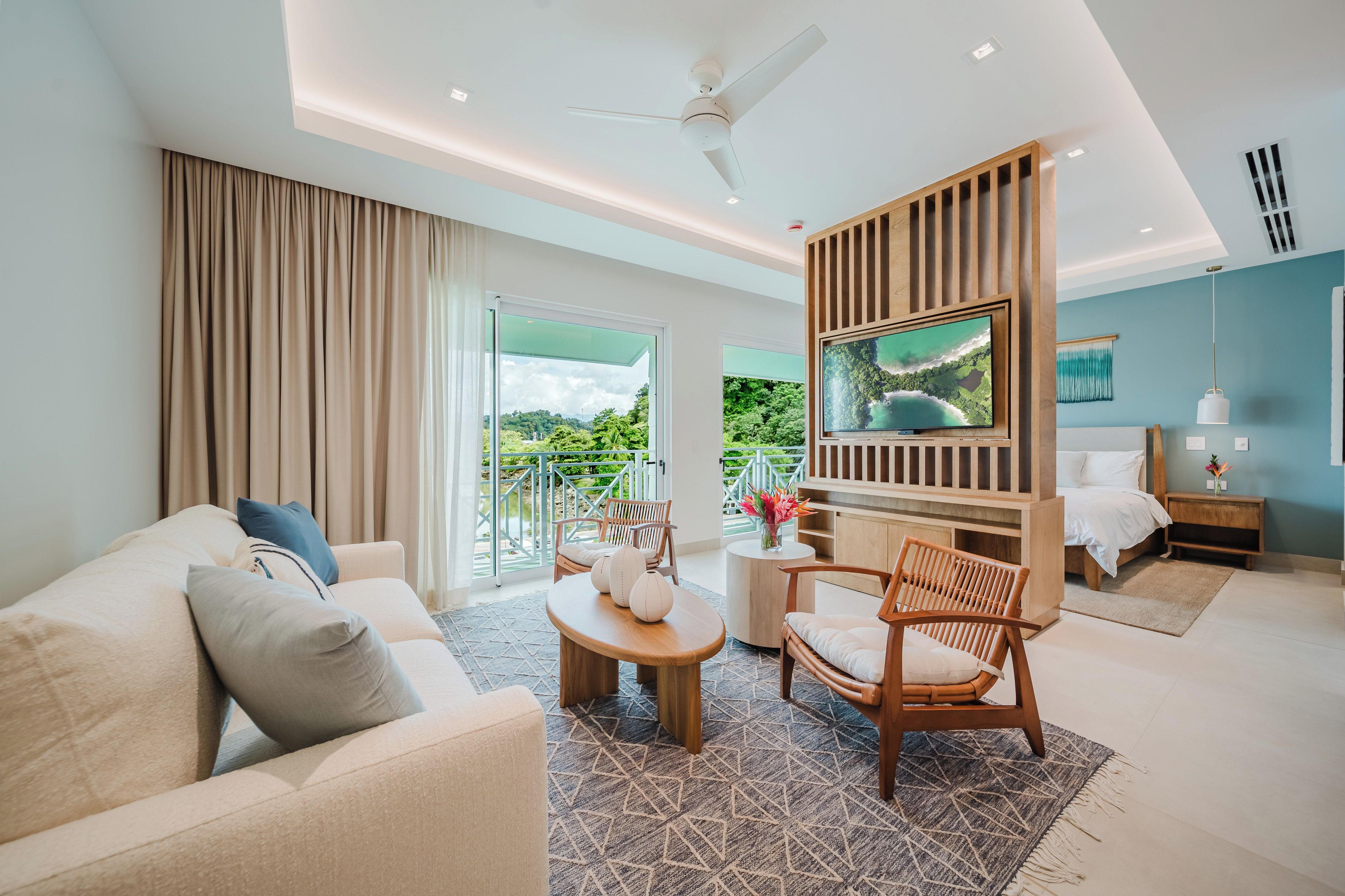 A modern hotel room with a balcony, a TV, a bed, a sofa, and a dining area.