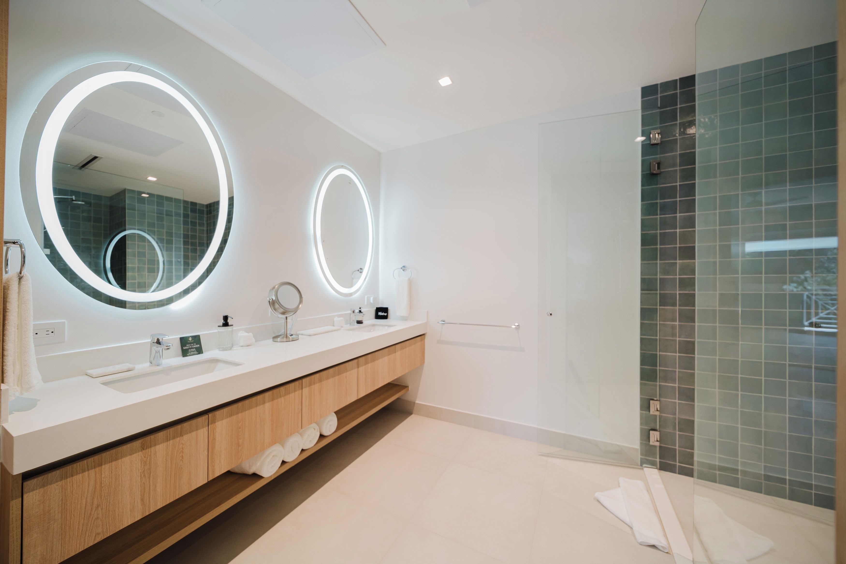 A modern bathroom with two large mirrors, a vanity with a sink, and a glass shower enclosure.
