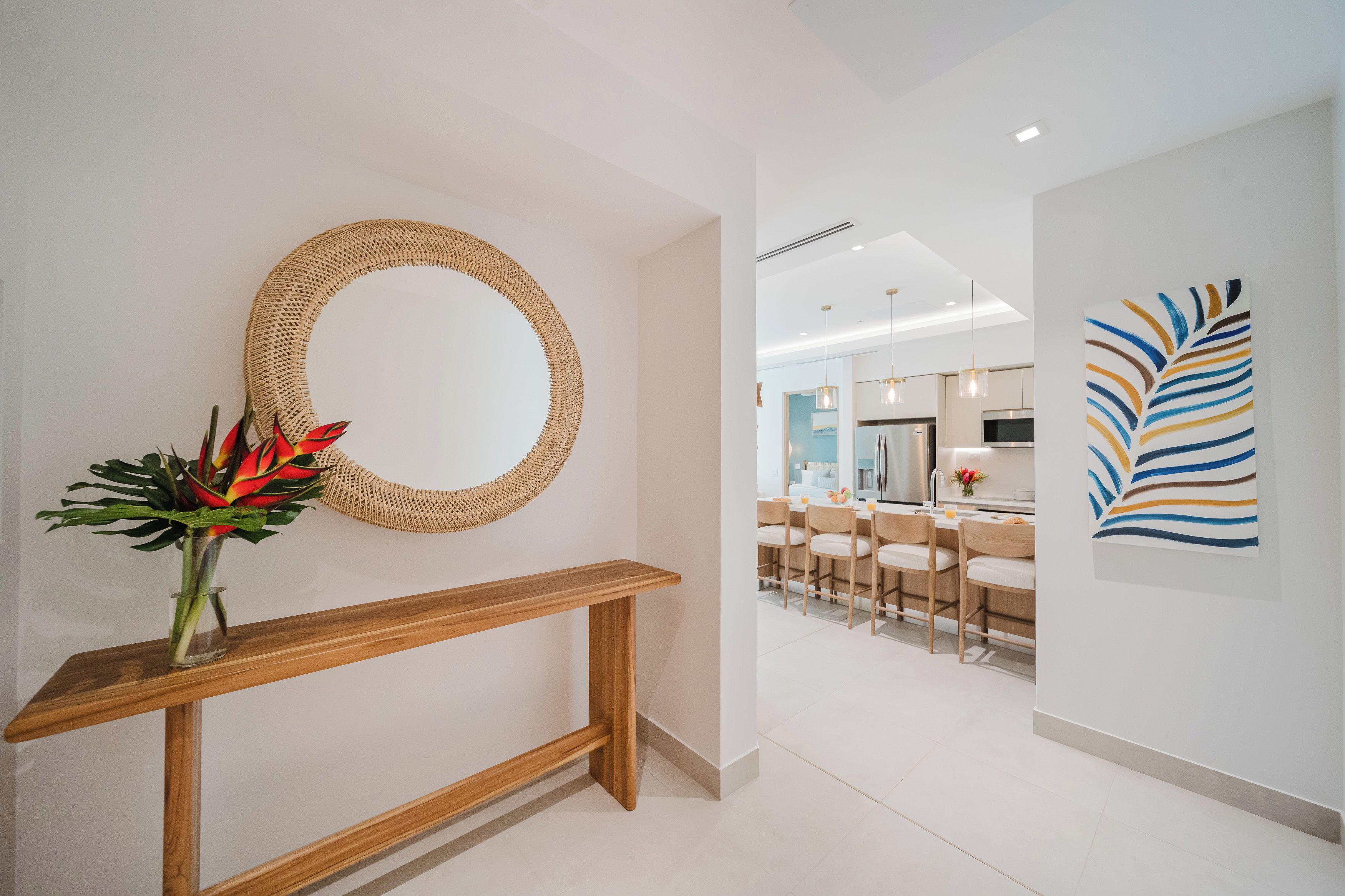 Un intérieur moderne agrémenté d’un grand miroir rond en fibres tressées, d’une console en bois et d’un coin repas avec des chaises et une table.