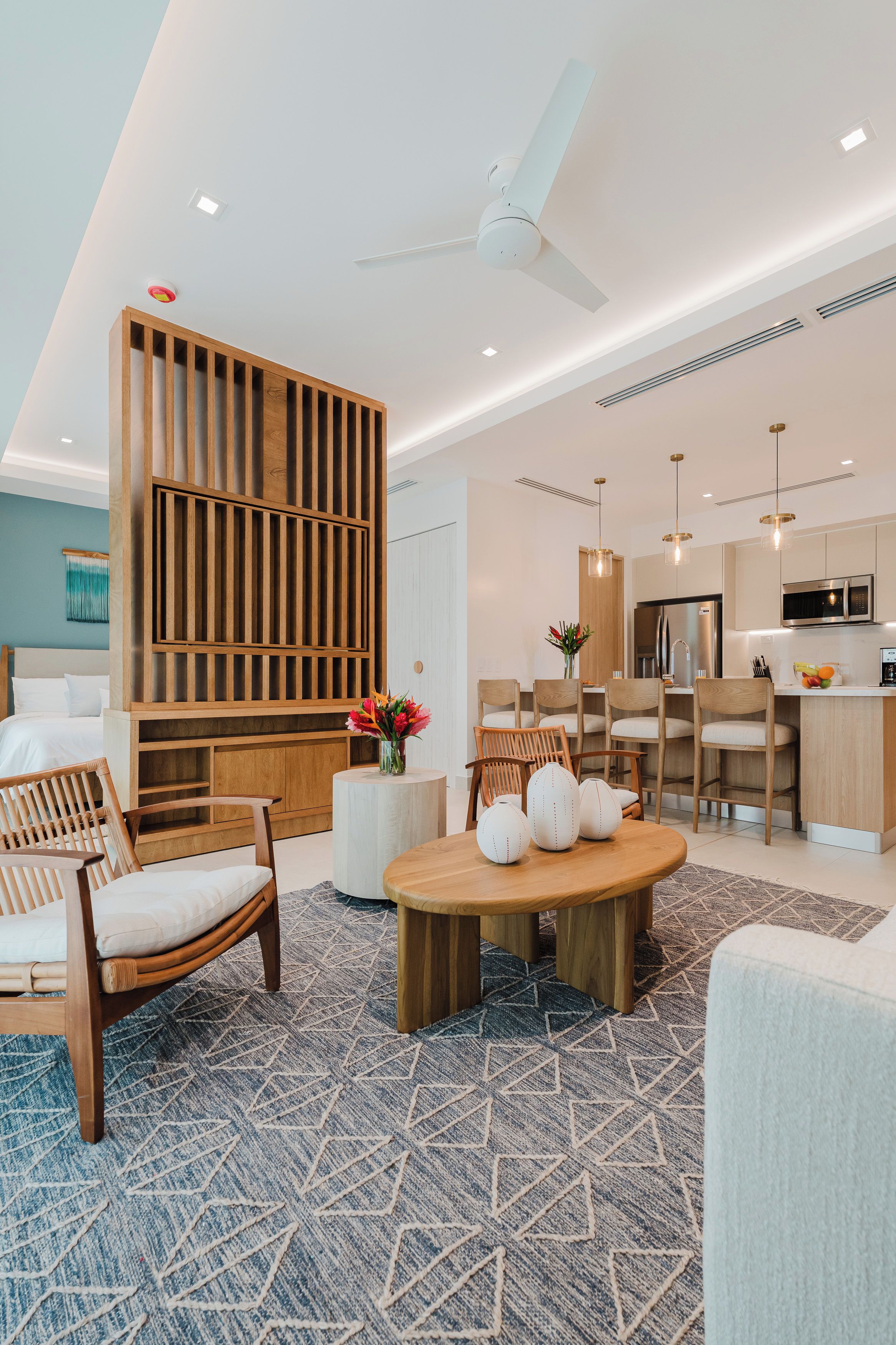 A modern living room with a wooden partition, a dining area with chairs, a round wooden table, and a kitchen with a microwave.