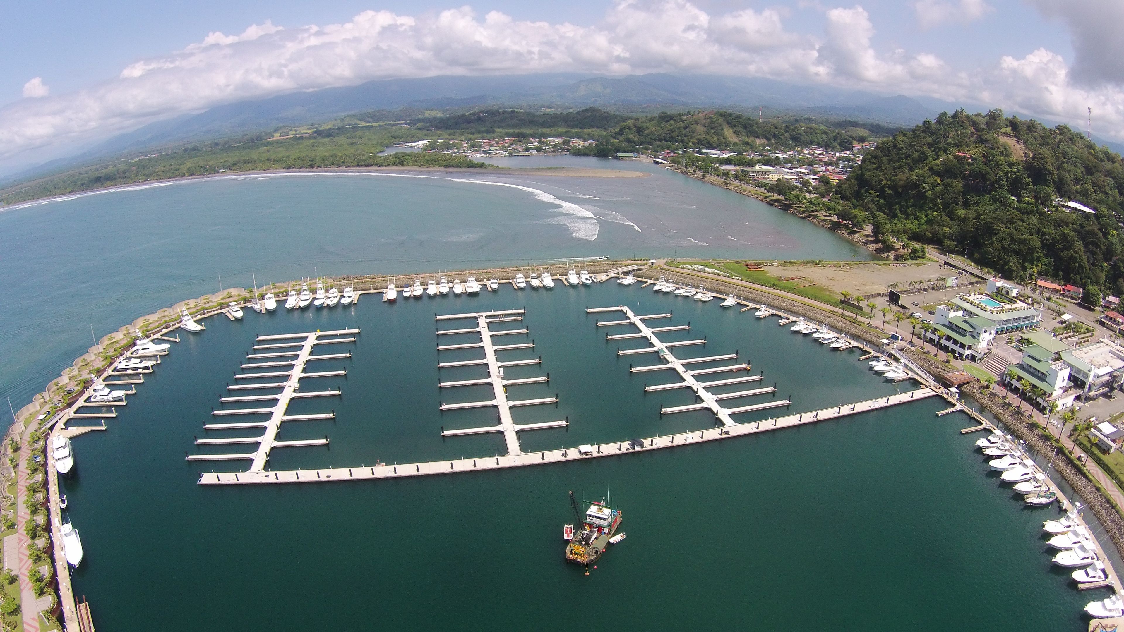 A marina with multiple docks and boats, surrounded by a coastal landscape with hills and a clear sky.