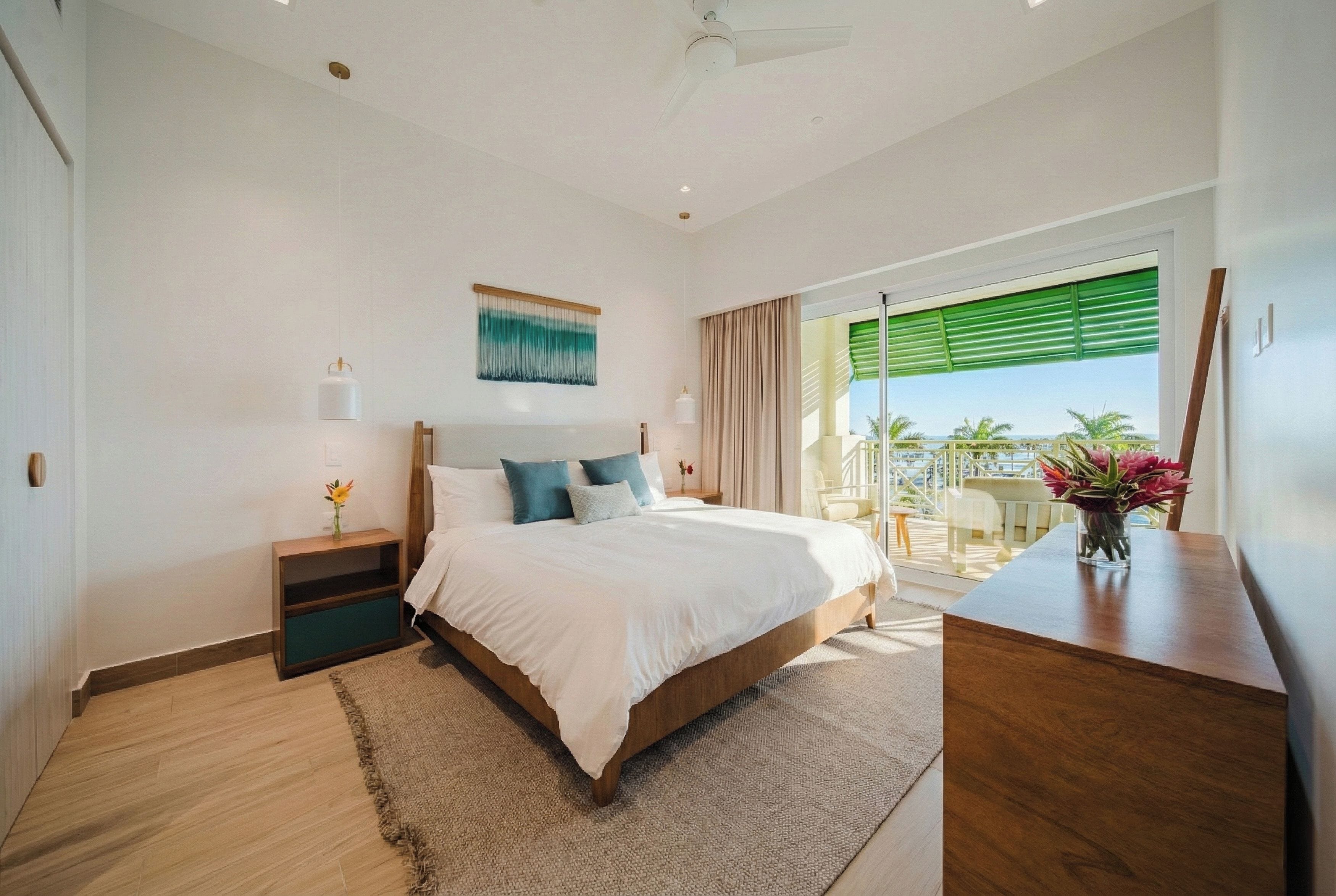 Une chambre à coucher comprenant un lit, des tables de chevet, un bureau, une vue sur l’extérieur et un ventilateur de plafond.