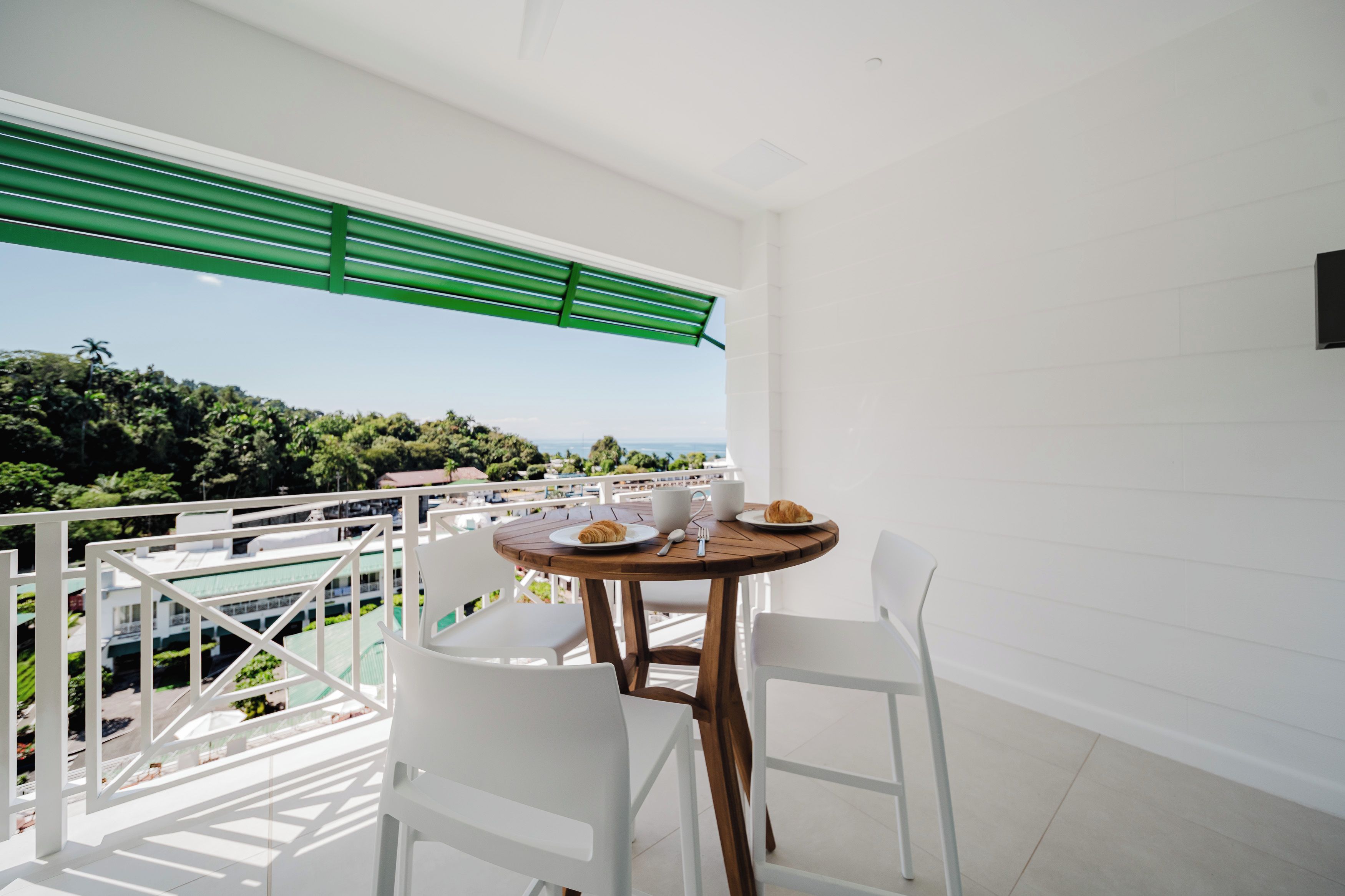 Un balcon avec une table et des chaises, offrant une vue sur un paysage luxuriant et la mer.
