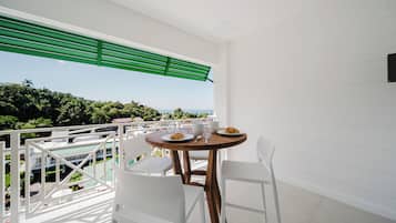 Un balcon avec une table et des chaises, offrant une vue sur un paysage luxuriant et la mer.