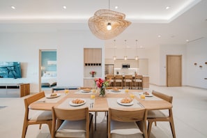 A modern dining area with a wooden table set for breakfast, a kitchen in the background, and a living area with a sofa and a TV. - Las Villas Marina Pez Vela  (Provincia de Puntarenas)