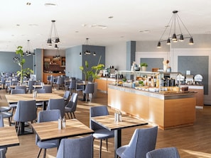 Een modern restaurant met verschillende eettafels en stoelen, een bar in het midden en verlichting in het plafond.