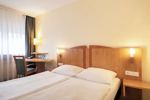 Een hotelkamer met een bed, een bureau, een stoel en twee bedlampjes.