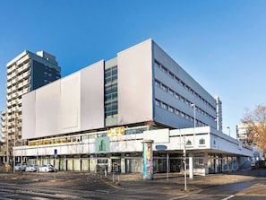 Een modern gebouw met een platte gevel, meerdere verdiepingen en een gelijkvloerse ingang met een bord waarop receptie en diensten staan.