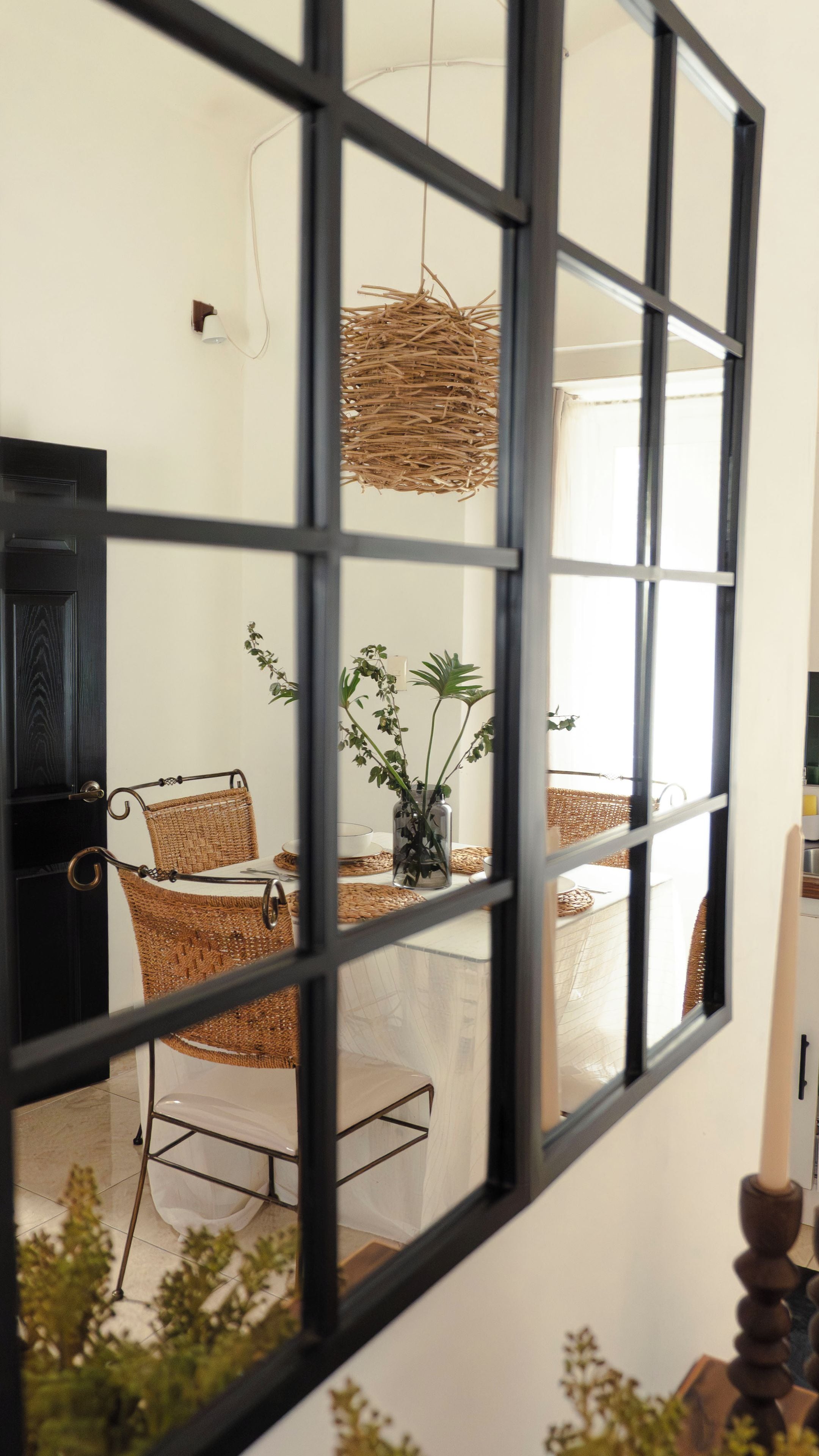 A room with a dining table, chairs, a hanging light fixture, and a window with a view of greenery outside.