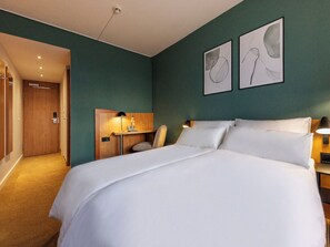 Ein Hotelzimmer mit einem großen Bett, einem Schreibtisch mit Lampe und Bildern an der Wand.