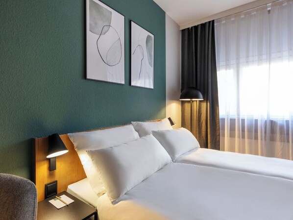 Een hotelkamer met een bed, een nachtkastje, een lamp en twee abstracte kunstwerken in lijsten aan de muur.
