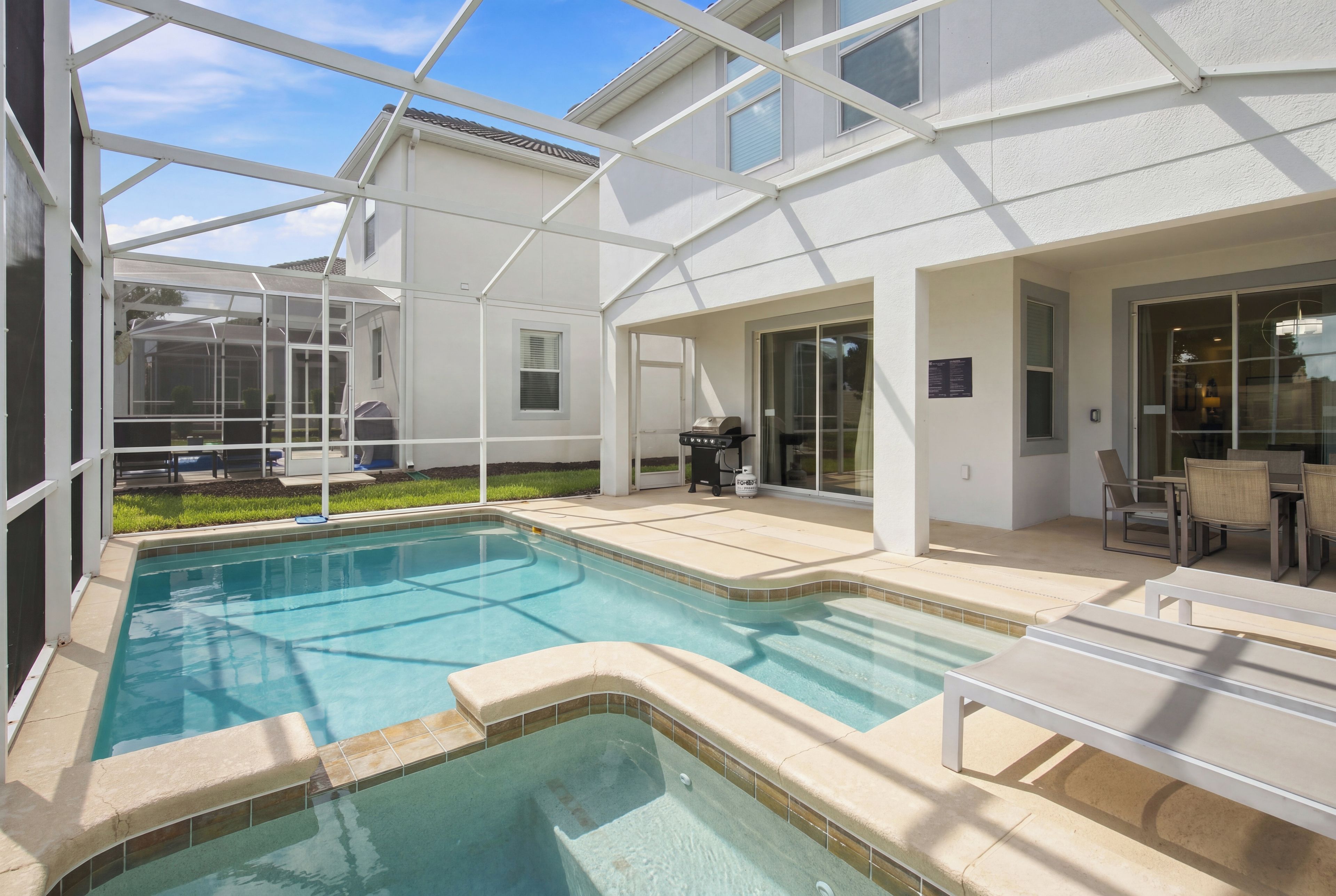 Une piscine dont le centre est plus profond que le reste, entourée d’une terrasse couverte aménagée avec du mobilier d’extérieur.