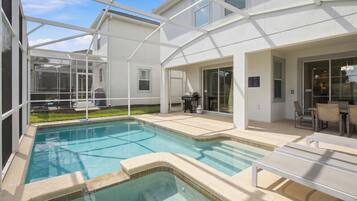 Une piscine dont le centre est plus profond que le reste, entourée d’une terrasse couverte aménagée avec du mobilier d’extérieur.