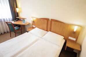 Ein Hotelzimmer mit einem Bett, einem Schreibtisch, einem Sessel und zwei Nachttischen mit Lampen.