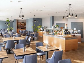 Een modern restaurant met verschillende eettafels en stoelen, een bar in het midden en verlichting in het plafond.