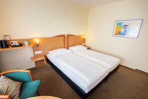 Een hotelkamer met een tweepersoonsbed, een bureau met lamp, een stoel en een wanddecoratie.