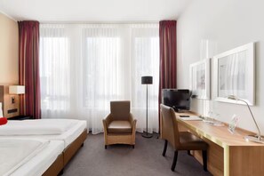 Een hotelkamer met twee bedden, een bureau met een computer, een stoel en een televisie.