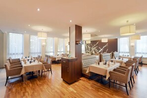 Een modern restaurant met houten vloeren, ronde tafels en comfortabele zitbanken.