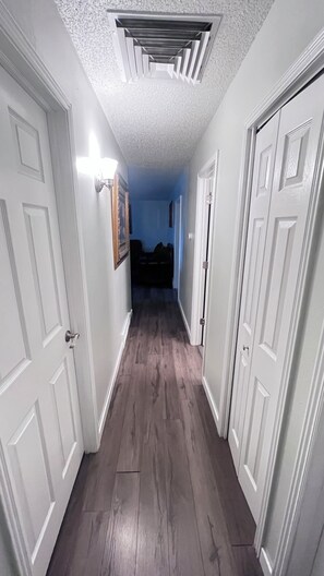 Corredor com portas brancas, luminária e piso de madeira escura.