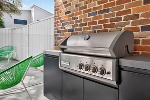 Ein Grill für den Außenbereich mit digitaler Anzeige, vor einer Ziegelwand mit weißem Zaun und grünen Stühlen.