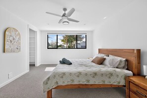 Una camera da letto con un letto, una ventola a soffitto, una finestra vista palme e una testiera in legno.