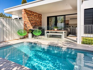 Ein Swimmingpool mit zwei Stühlen, einem Tisch und einem Grill.