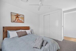 Ein Schlafzimmer mit Bett, Kissen, Deckenventilator, einer Tür und einem Bild an der Wand.