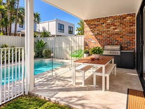 Un patio con piscina, un tavolo in legno e un barbecue.