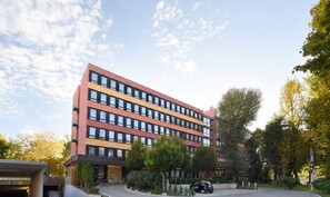 Een meerlaags hotel met een modern design, met een binnentuin met bomen en een parkeerplaats.